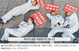 「健康睡眠」などのプラカードを並べ、パジャマ姿で路上に寝転ぶ中国の若者たち。自らを「躺平族(寝そべり族)」と呼ぶ若者の姿