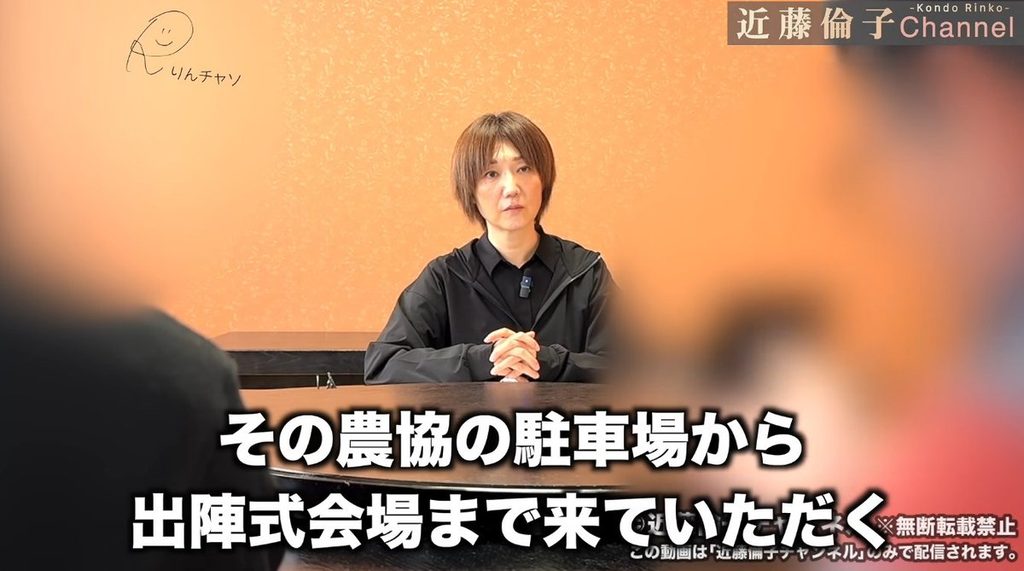 近藤倫子さんが関係者に取材する場面。農協の駐車場に車を停めてもらい、そこから出陣式の会場まで来てもらう流れが説明されている。